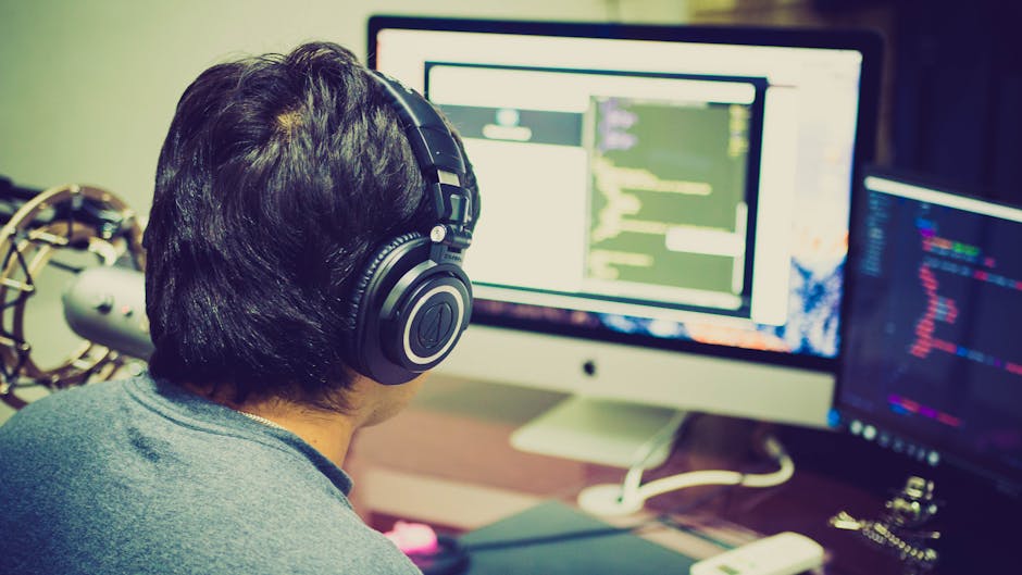 A programmer with headphones focuses on coding at a computer setup with dual monitors